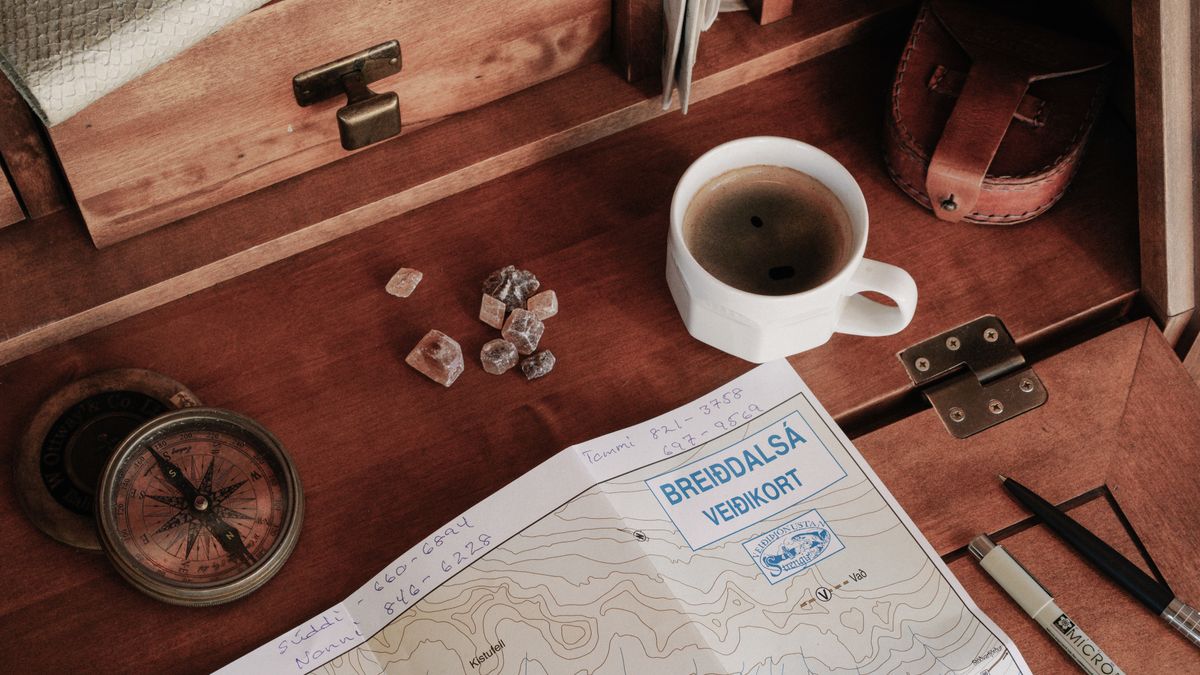 A top-down view of a rustic workspace featuring a map, compass, and a cup of coffee.