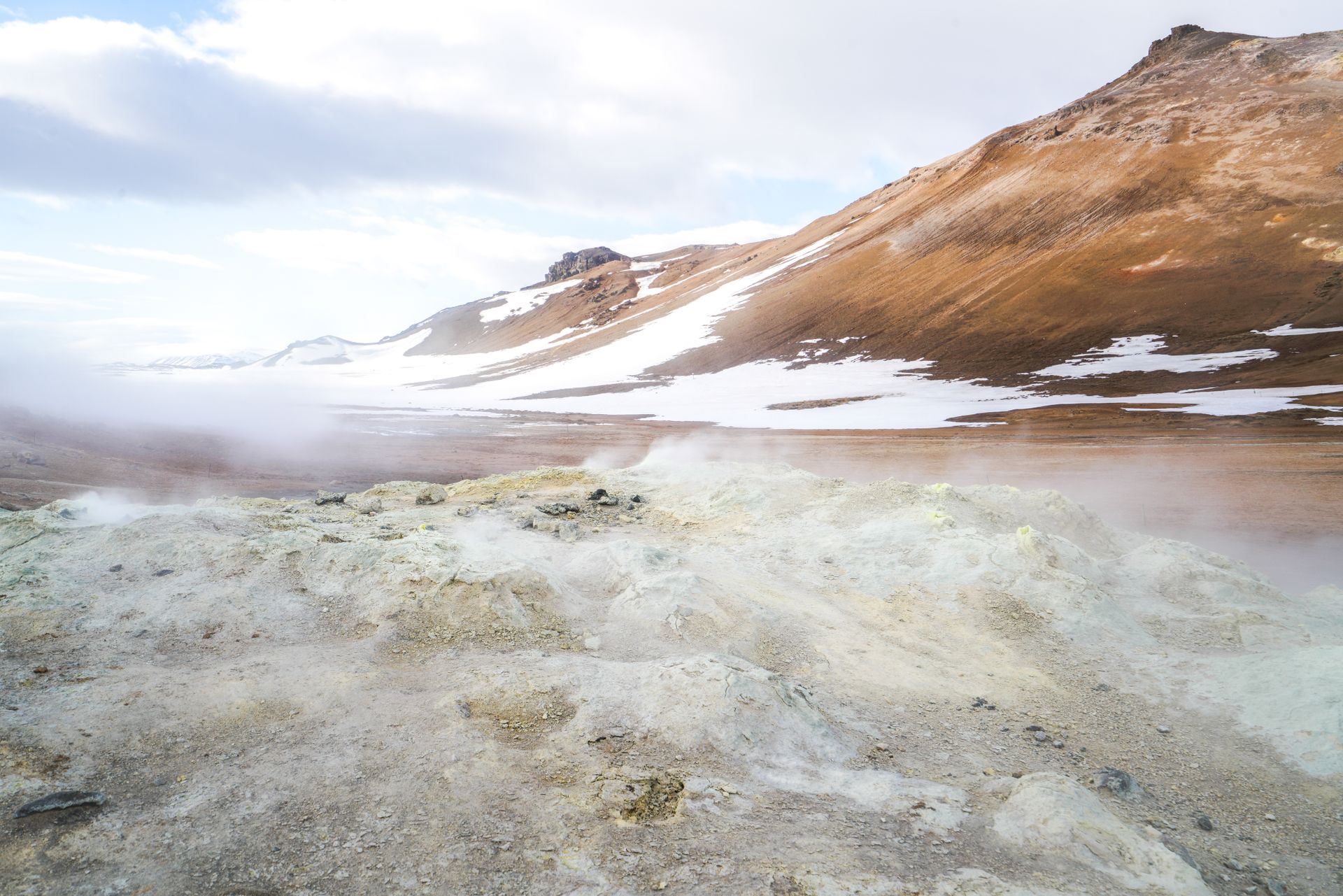 Explore the stunning geothermal landscape of Iceland with steaming terrain and snowy mountains.