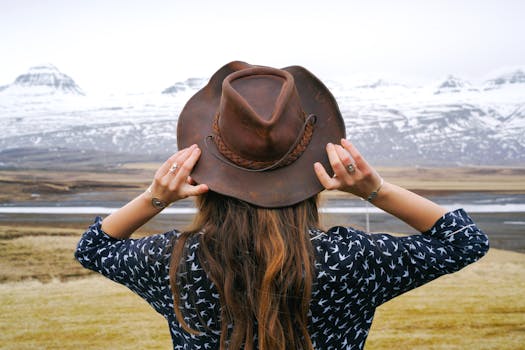 A woman with a cowboy hat gazes at snow-capped mountains, embracing nature's beauty.