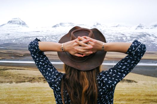 A woman with a cowboy hat gazes at a scenic mountain view, embodying tranquility and adventure.