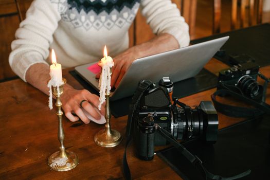 A cozy setting featuring a photographer working on a laptop, surrounded by cameras and candlelight.