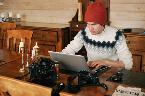 A Man Sitting at a Wooden Table Using a Laptop 