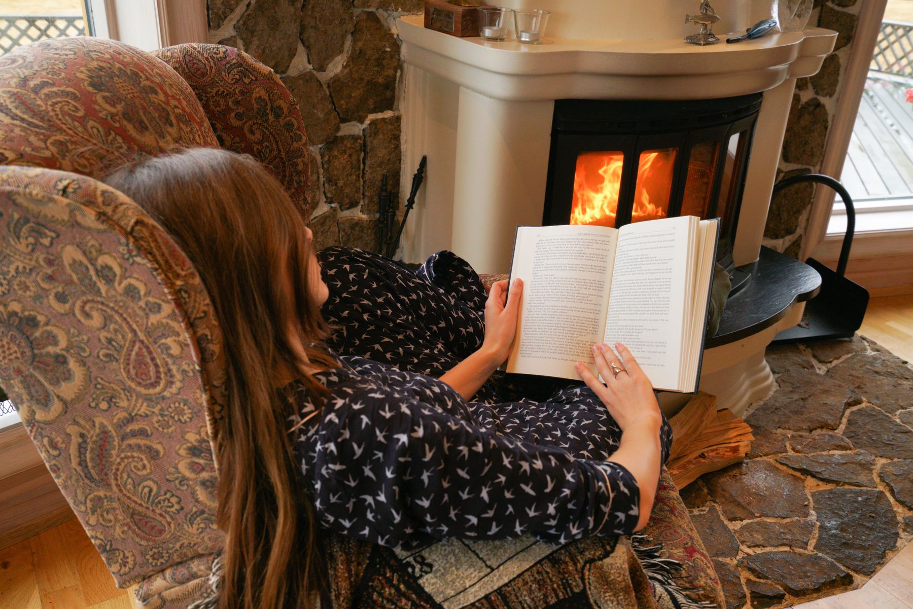 A guest reading by the stone fireplace in a cozy armchair