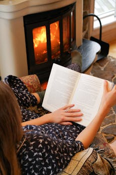 Woman relaxing and reading by fire, creating a cozy atmosphere with warm ambiance.