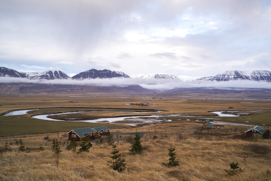 Breathtaking landscape of a winding river through a valley with snow-capped mountains and scattered houses.