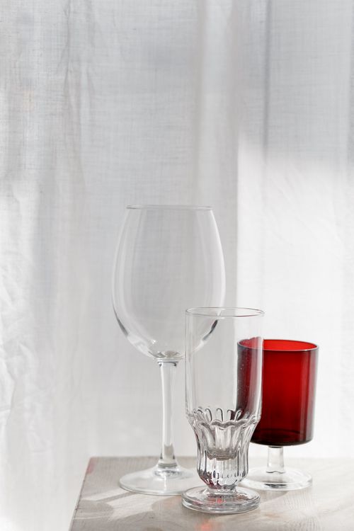 Free A minimalist still life showing clear and red glassware on a white surface with curtains. Stock Photo