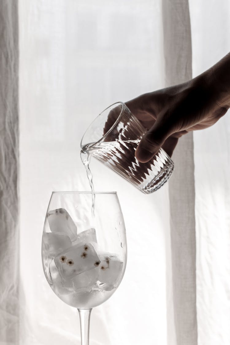 A Hand Pouring Water On A Wine Glass