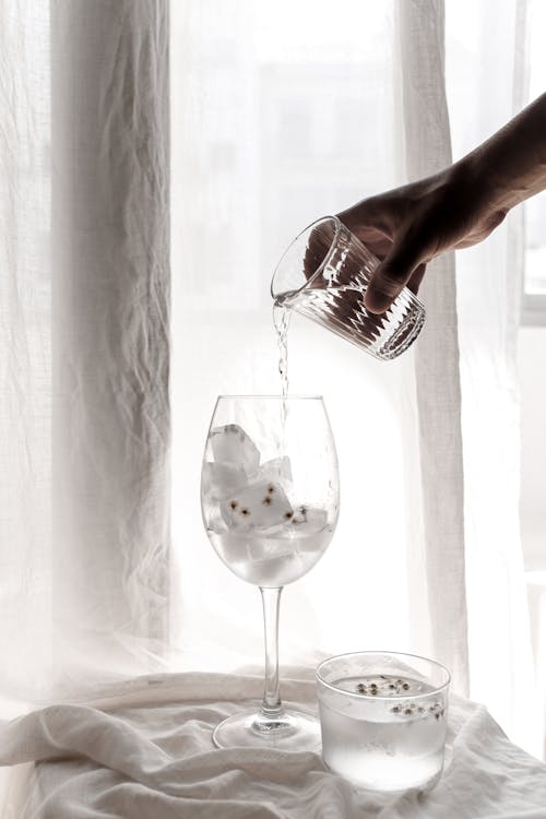 A Hand Pouring Water on a Wine Glass with Ice Cubes