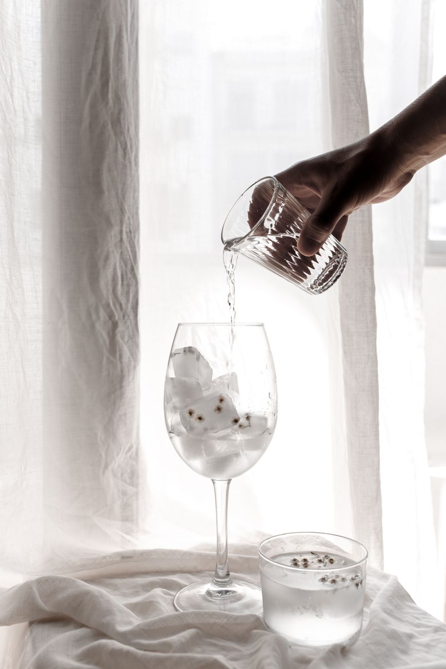 A minimalistic scene capturing water being poured into a wine glass with ice cubes.