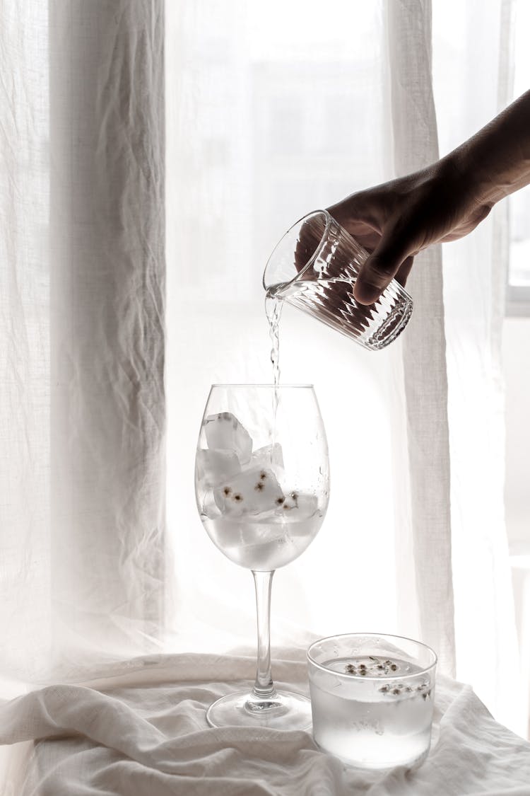 A Hand Pouring Water On A Wine Glass With Ice Cubes