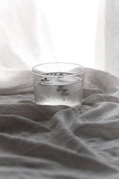 白色纺织品背景上，透明玻璃杯盛着冰水，传递出清新的感觉