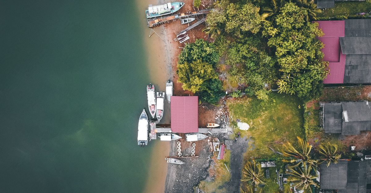 Picturesque aerial view of boats moored on sea near sandy coast surrounded by green tropical trees and typical houses