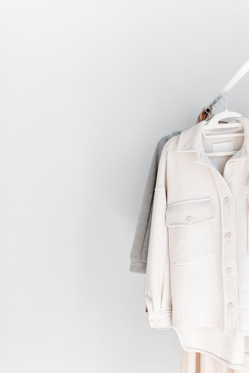 A minimalist wardrobe featuring neutral-tone clothes on hangers against a white background.