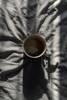 在柔和光线下，咖啡杯的顶视图在织物上投下戏剧性的阴影