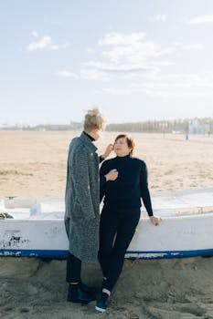 Two adults share a tender moment at the beach by a boat on a sunny day.