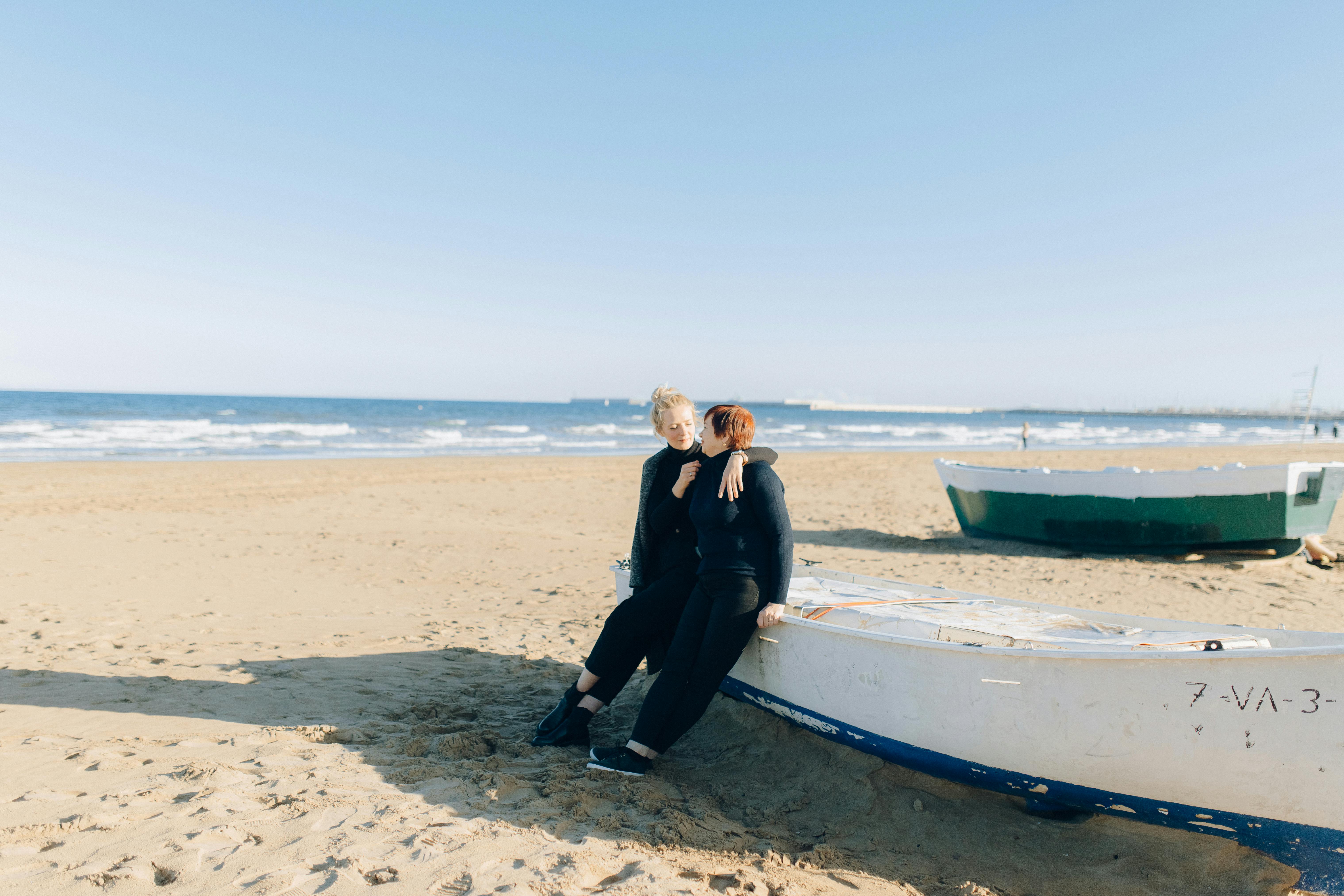 man in black suit standing beside blue and white boat on beach