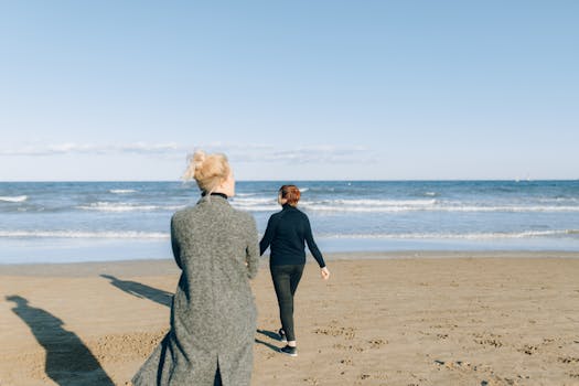 A couple enjoys a peaceful walk on a sandy beach with an ocean view during sunrise.
