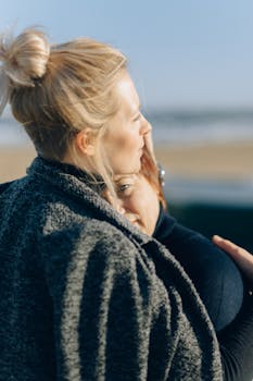 Mother and daughter share a cozy hug by the beach on a sunny day.