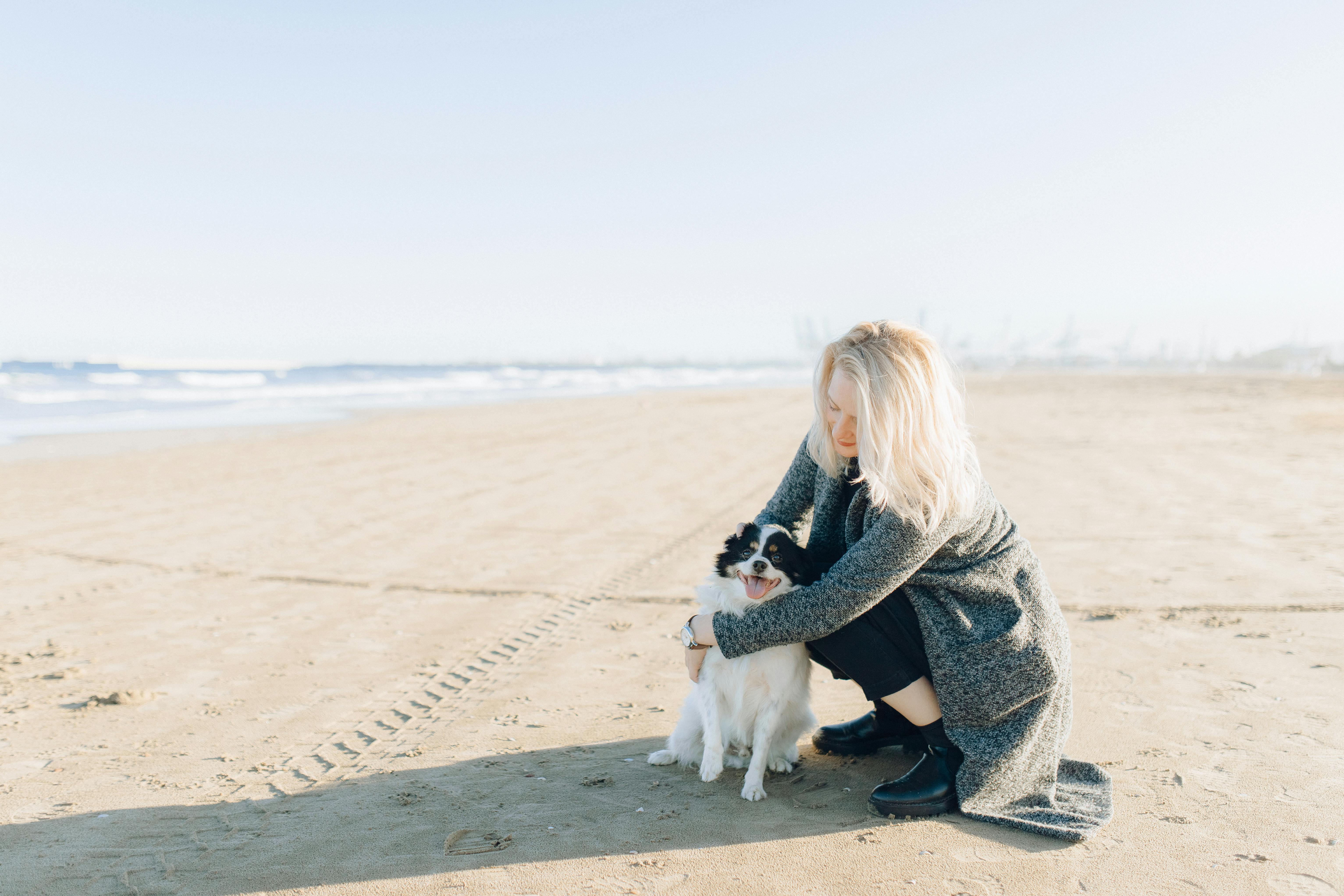 woman in gray sweater sitting on gray concrete floor beside white short coated dog