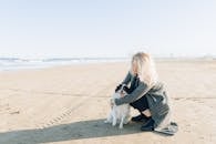 一位妇女穿着长外套，在阳光明媚的海滩上抱着她的狗，享受着平静的一天