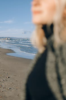 A person blurred in focus with a sunny beach and waves in background, capturing a serene moment.
