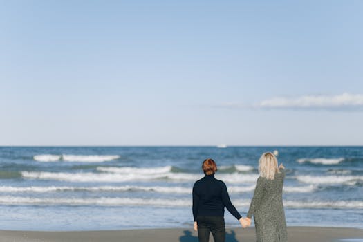 A romantic scene of a couple holding hands while enjoying a walk by the sea on a sunny day.
