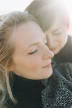 Close-up of two women sharing a tender embrace in natural lighting outdoors.