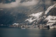 从空中俯瞰冬季的湖镇，白雪皑皑的山脉环绕，景色宁静如画