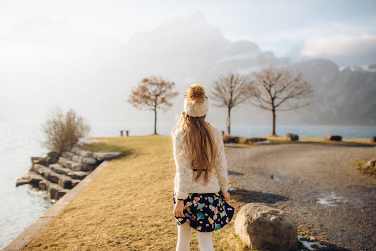 Young Woman In White Sweater And Floral Skirt Walking On A Park