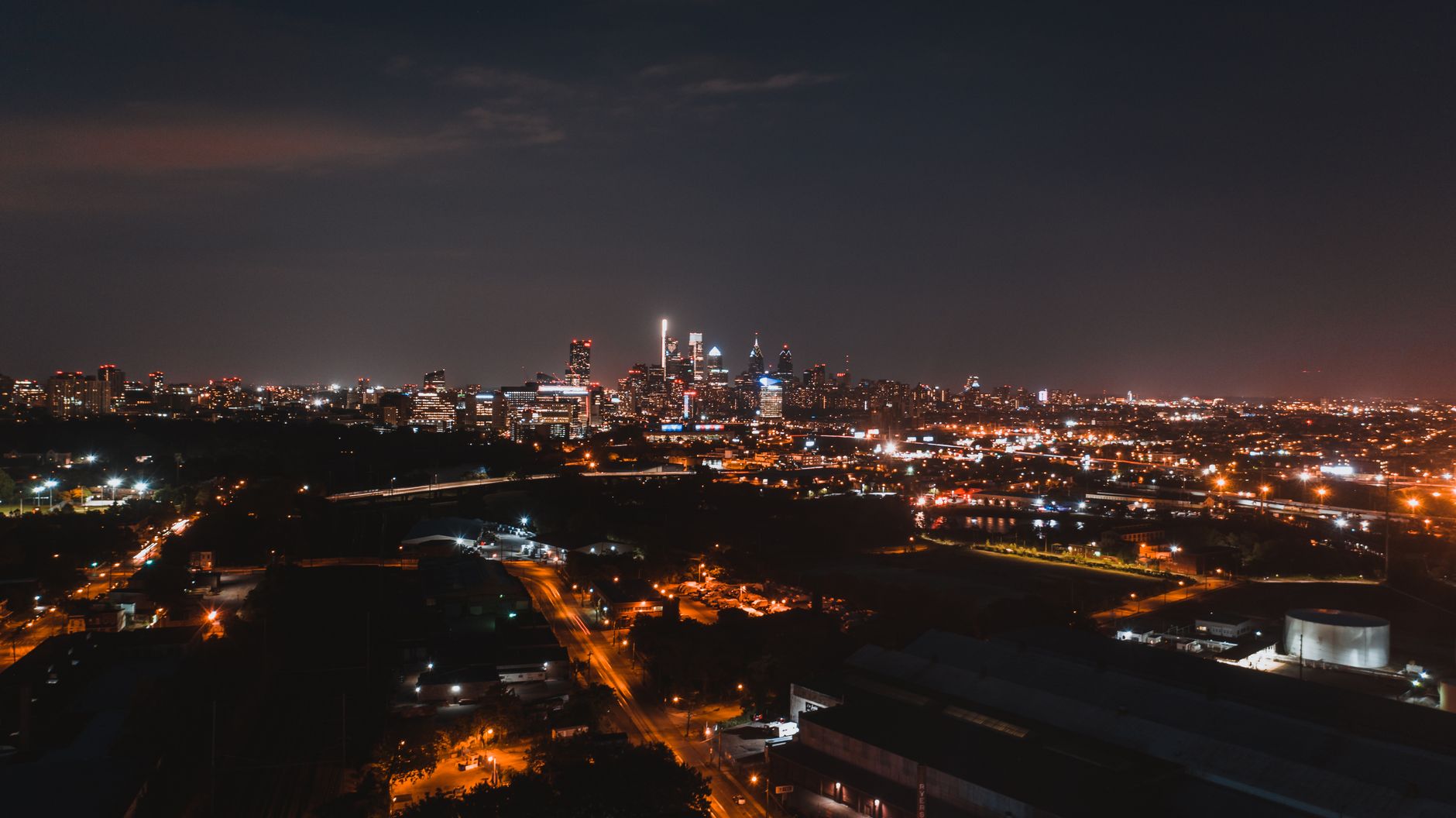 Bright lights shining on streets of modern city with skyscrapers and silhouettes of buildings at night