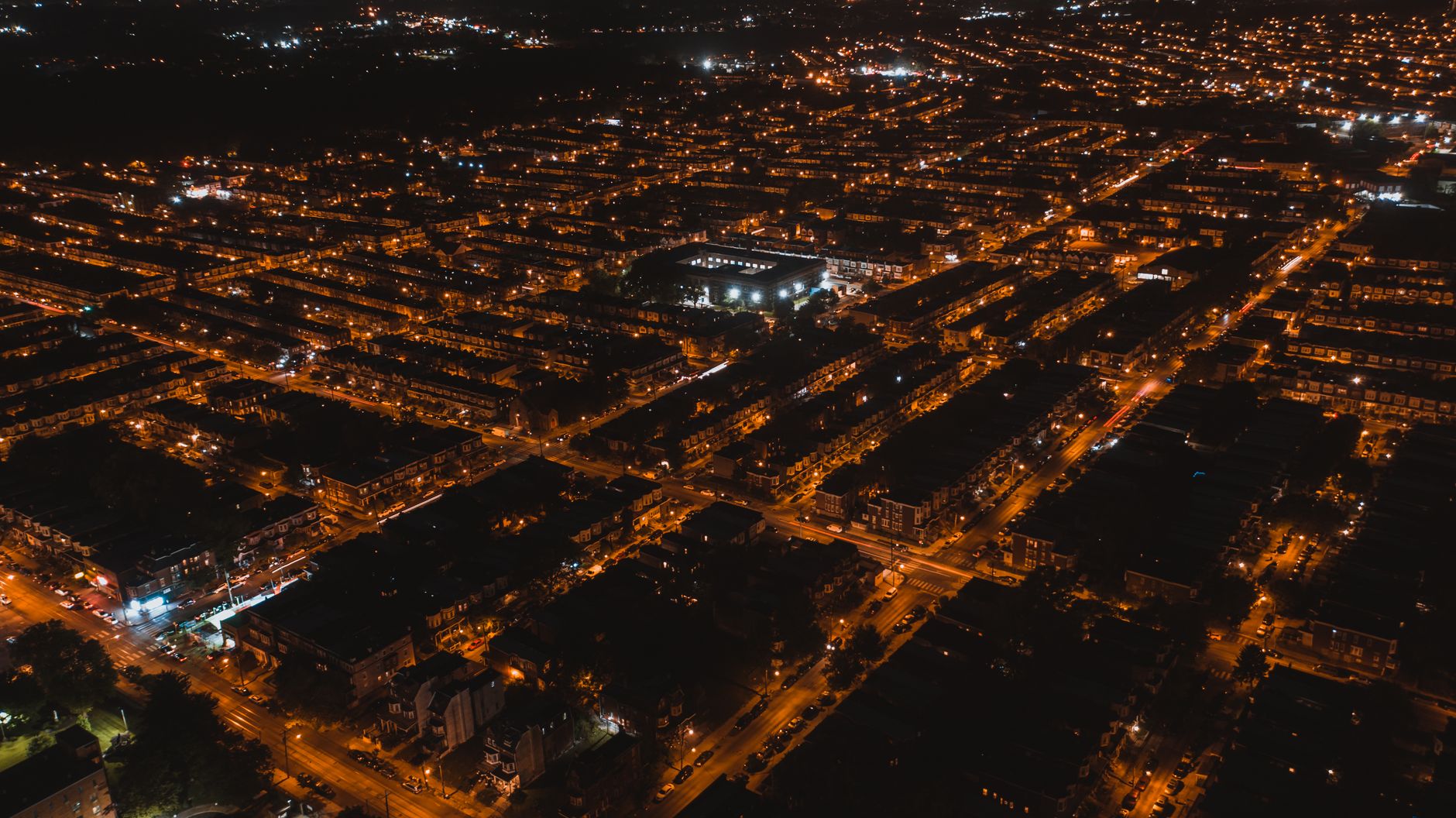 Aerial view of brightly illuminated streets of settlement with silhouettes of buildings at dark night
