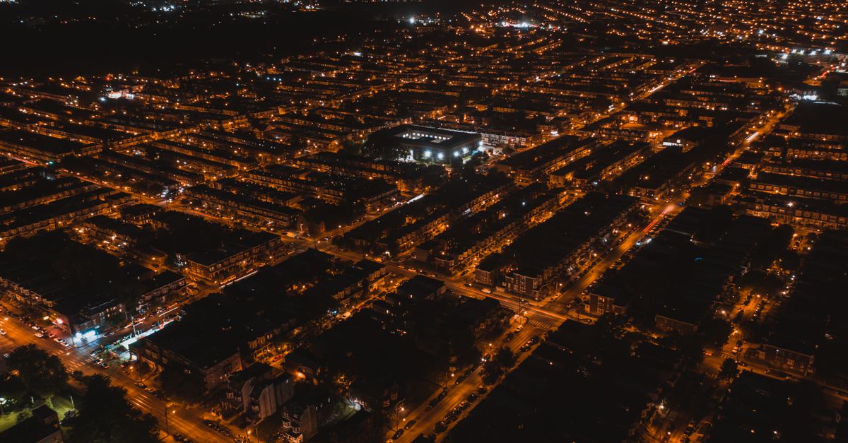 Aerial view of brightly illuminated streets of settlement with silhouettes of buildings at dark night