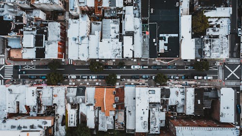 Aerial view of cars moving on city street surrounded by houses with white roofs in residential district