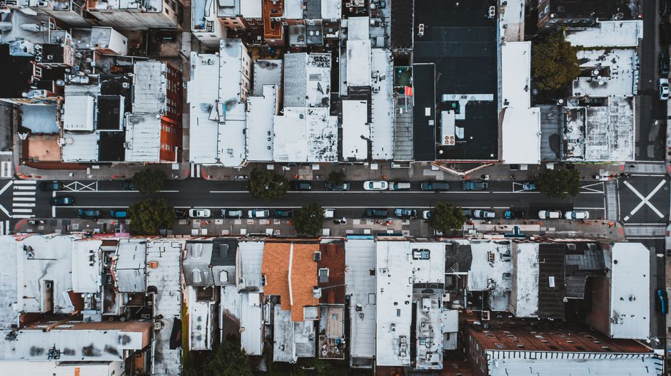 Aerial view of cars moving on city street surrounded by houses with white roofs in residential district