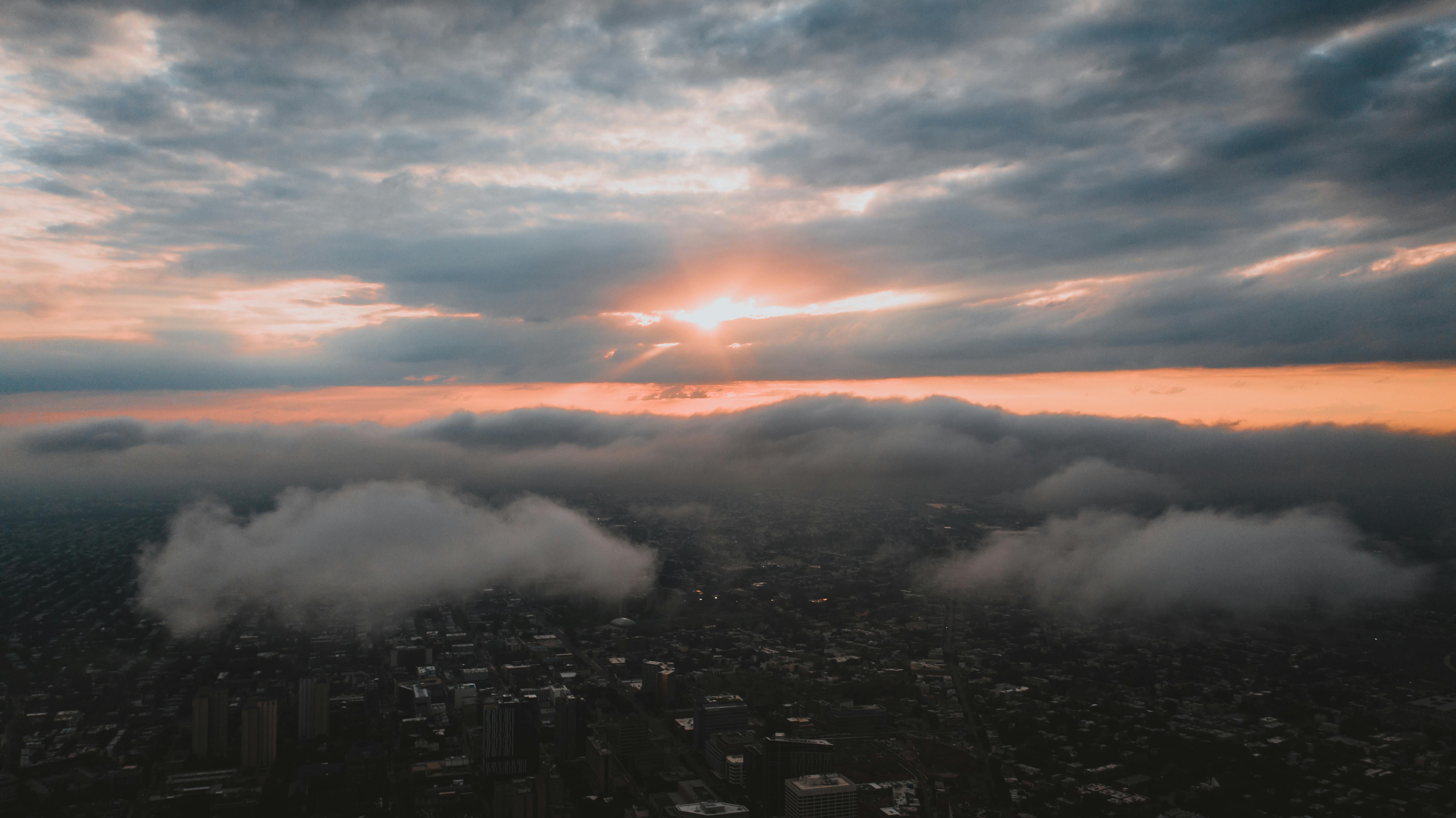 Aerial view of bright sunshine glowing through fluffy clouds floating over modern megapolis in sundown
