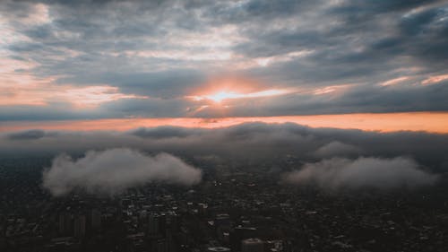 Free Aerial view of bright sunshine glowing through fluffy clouds floating over modern megapolis in sundown Stock Photo