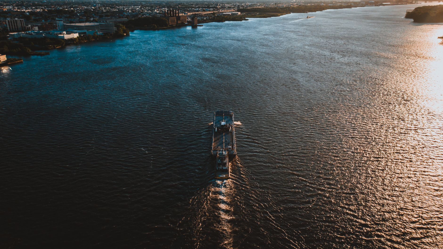 Drone view of ship floating on rippling water surface in sunny day and moving towards coastal city