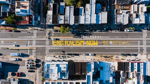 Free Overhead view of asphalt roadway with vehicles between building roofs and colorful title about racism Stock Photo