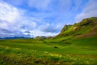 广阔的绿色山谷上方，明亮的蓝天映衬着戏剧性的山景