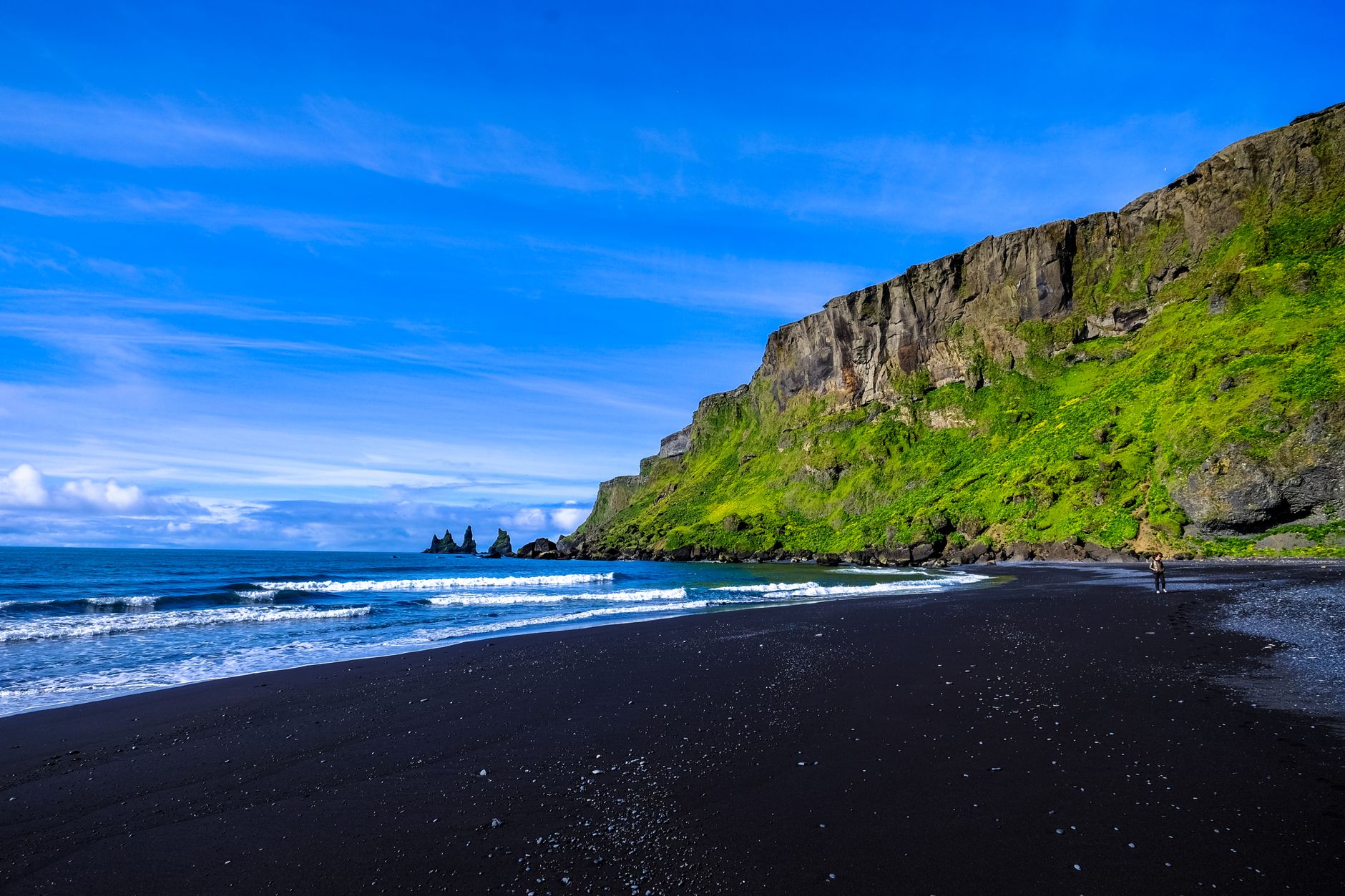 Explore a breathtaking black sand beach with towering cliffs and vibrant green moss, set against the blue ocean and sky.. pex