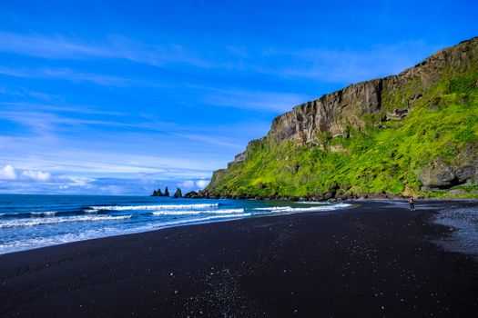 Explore a breathtaking black sand beach with towering cliffs and vibrant green moss, set against the blue ocean and sky.. pex
