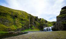 宁静的瀑布从冰岛郁郁葱葱的青山上倾泻而下，展现了大自然的宁静之美