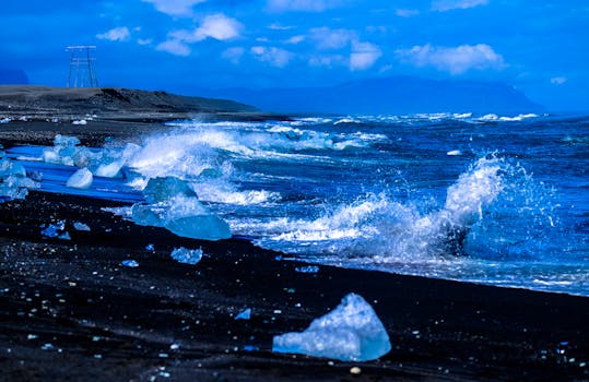Blue hues dominate this dramatic coastal scene with ice chunks and crashing waves against a dynamic sky.