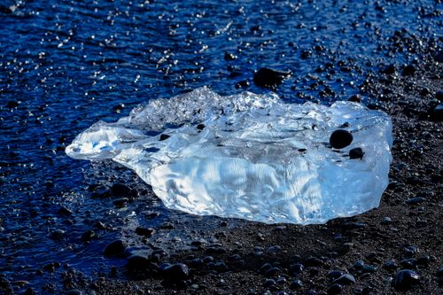 Free A shimmering iceberg on a rocky seashore, showcasing nature's icy beauty. Stock Photo