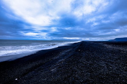 A mesmerizing view of a black sand beach with dramatic clouds and crashing waves, creating a serene atmosphere.