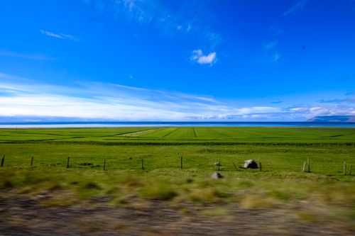 Free Vast green farmland under a vibrant blue sky, showcasing a tranquil rural scene. Stock Photo