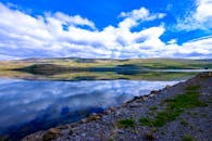宁静的山间湖泊倒映着蓝天和云层，周围环绕着大自然，景色迷人