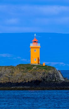在蓝天和海洋的背景下，一座充满活力的橙色灯塔矗立在岩石海岸线上