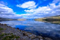 平静的湖泊倒映着云彩和天空，四周环绕着岩石海岸和远方的山脉，展现出宁静之美