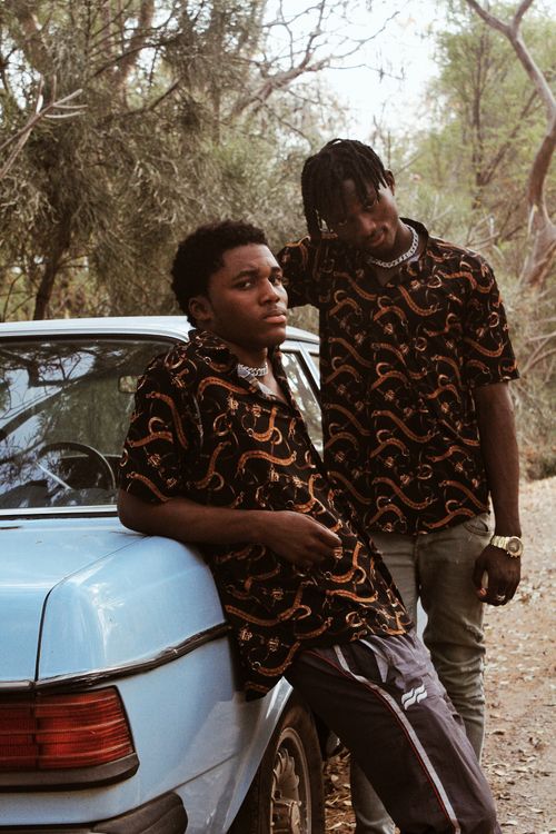 Free Young African American men with black hair in stylish clothes standing near car against tree in sunny day Stock Photo